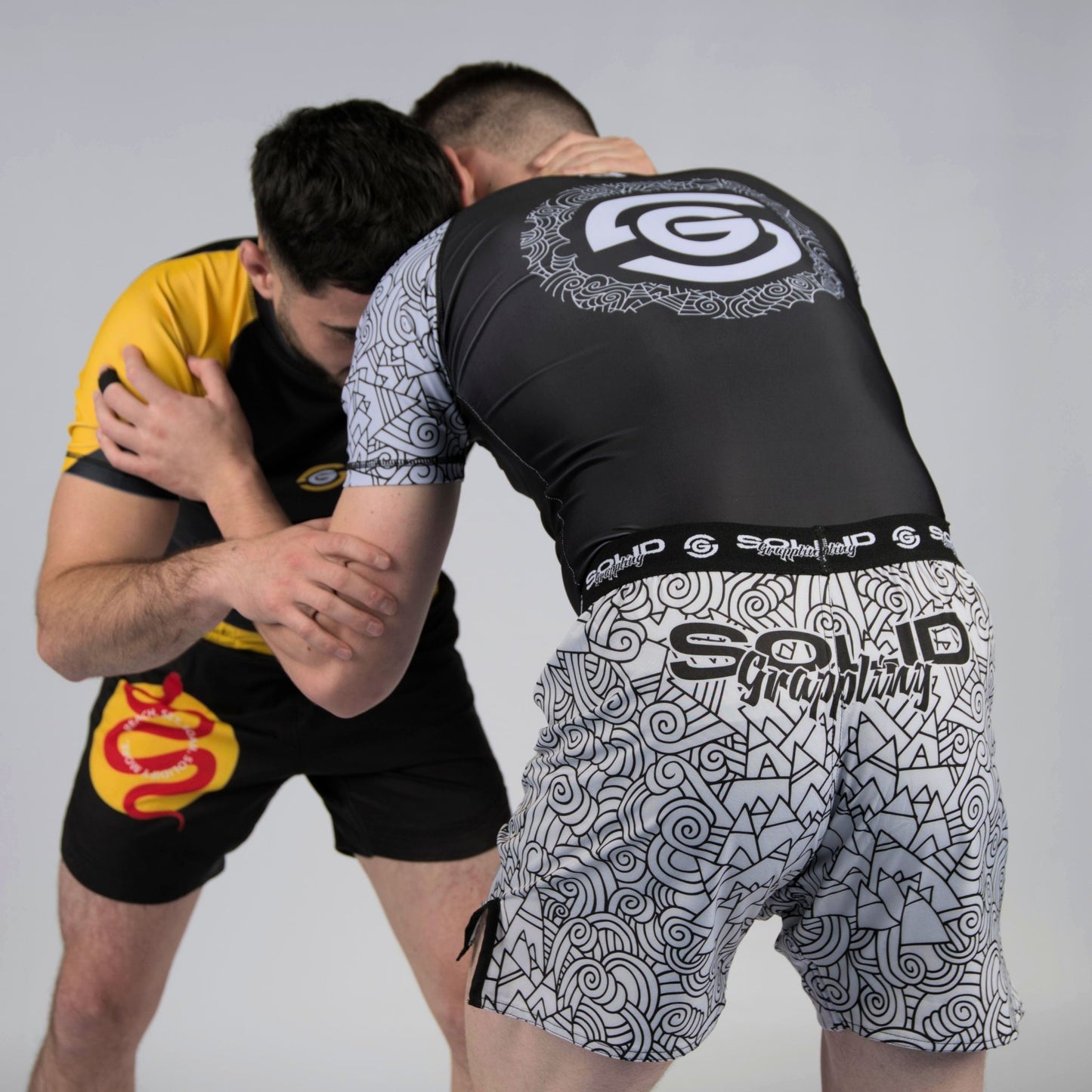 two men wearing solid grappling uk aztec and yellow vipers sits hand fighting for underhook